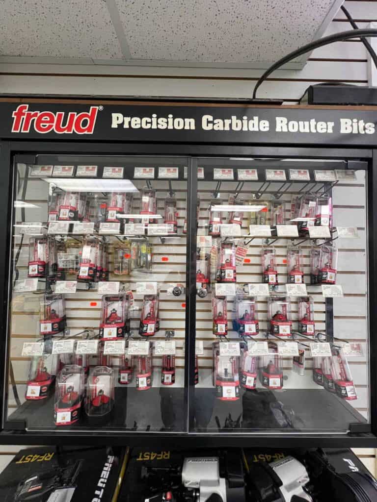 At Scott's Hill Hardware, a display case filled with various Freud precision carbide router bits showcases different types and sizes against a labeled backdrop reading "Freud Precision Carbide Router Bits.