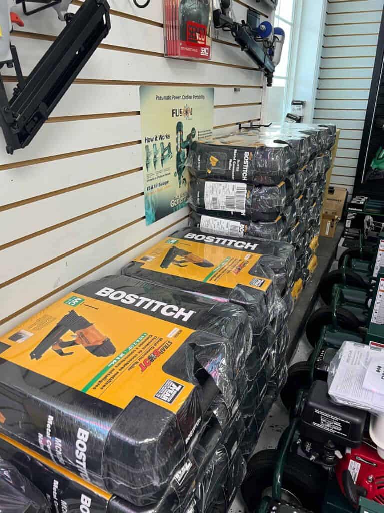 Stacked Bostitch pneumatic nailers packaged in plastic are prominently on display at Scott's Hill Hardware, with a poster on the wall and boxes of other tools visible nearby.