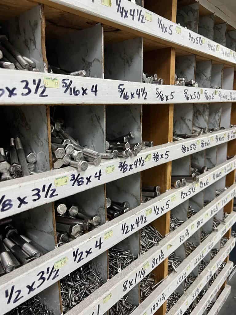 Organized shelving unit from Scott's Hill Hardware containing various sizes of bolts and screws, each compartment labeled with dimension markings.