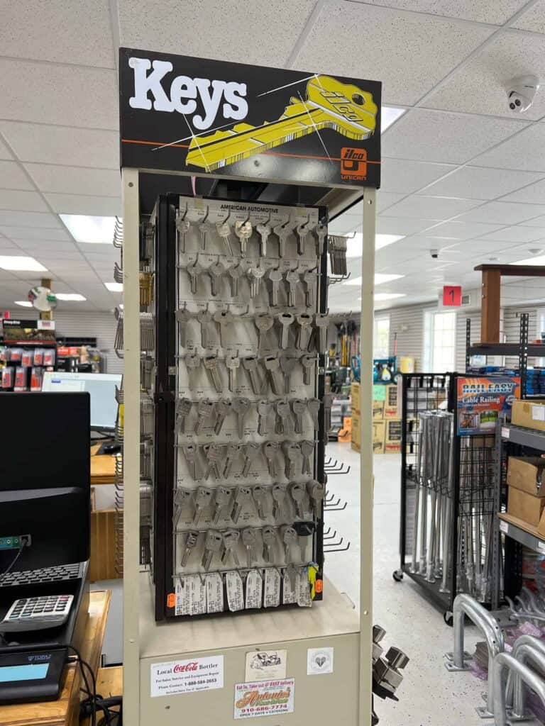 A display stand in Scott's Hill Hardware holds various key blanks for cutting. The sign at the top reads "Keys." The background shows additional store shelves and products.