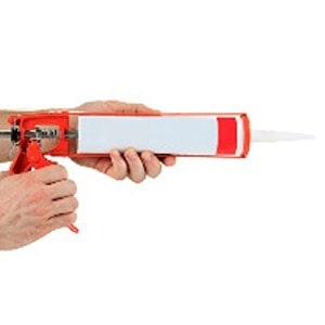 Hands holding a red and white caulking gun, with a tube of sealant inside, ready for use from Scott's Hill Hardware.