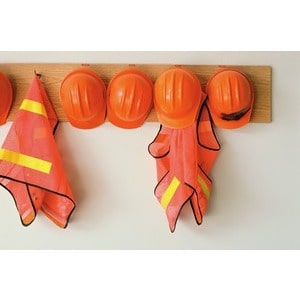 Four orange hard hats and two orange safety vests with yellow reflective stripes hang on a wooden rack at Scott's Hill Hardware.